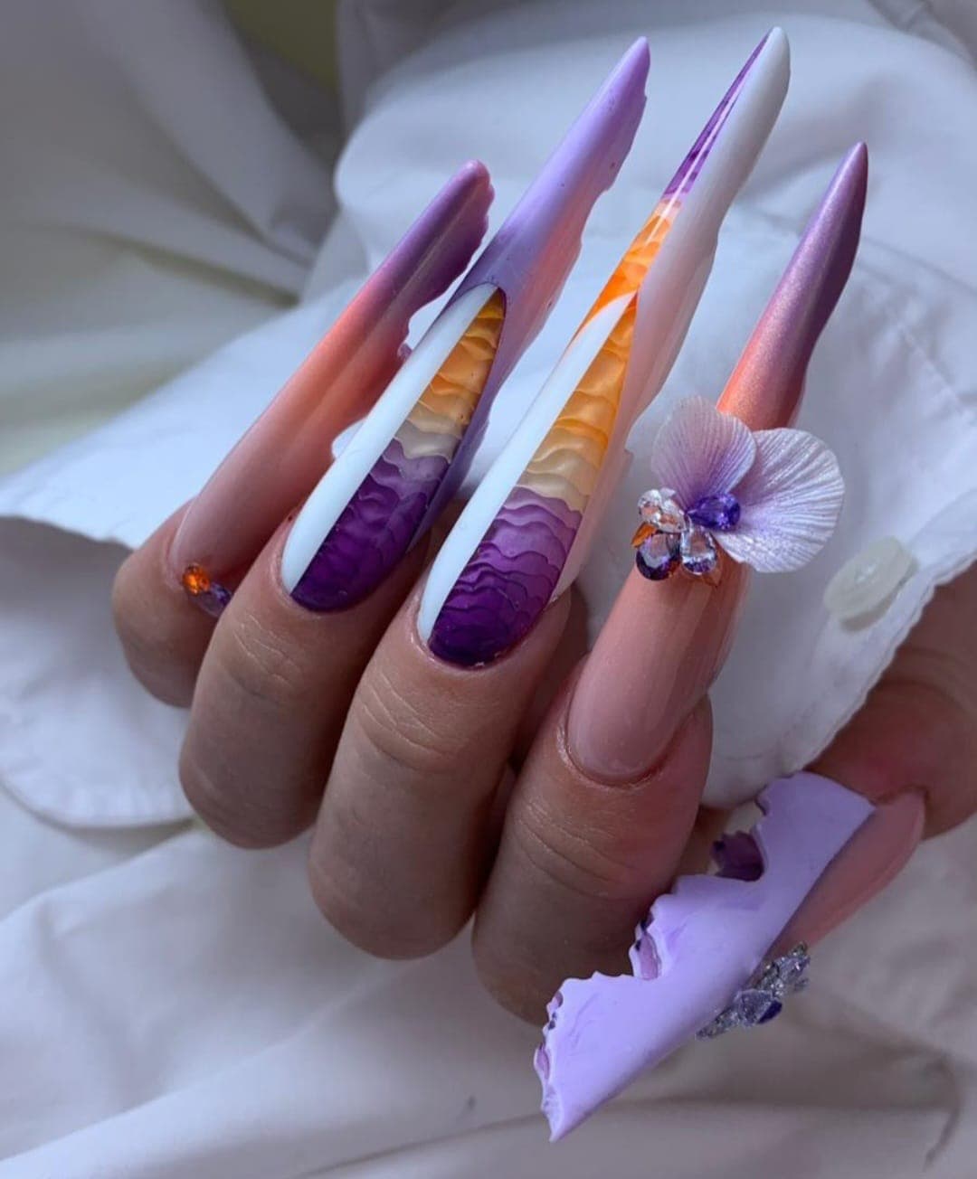 Unhas stiletto compridas com design degradê roxo e laranja, efeito marmoreado, aplicações 3D e strass