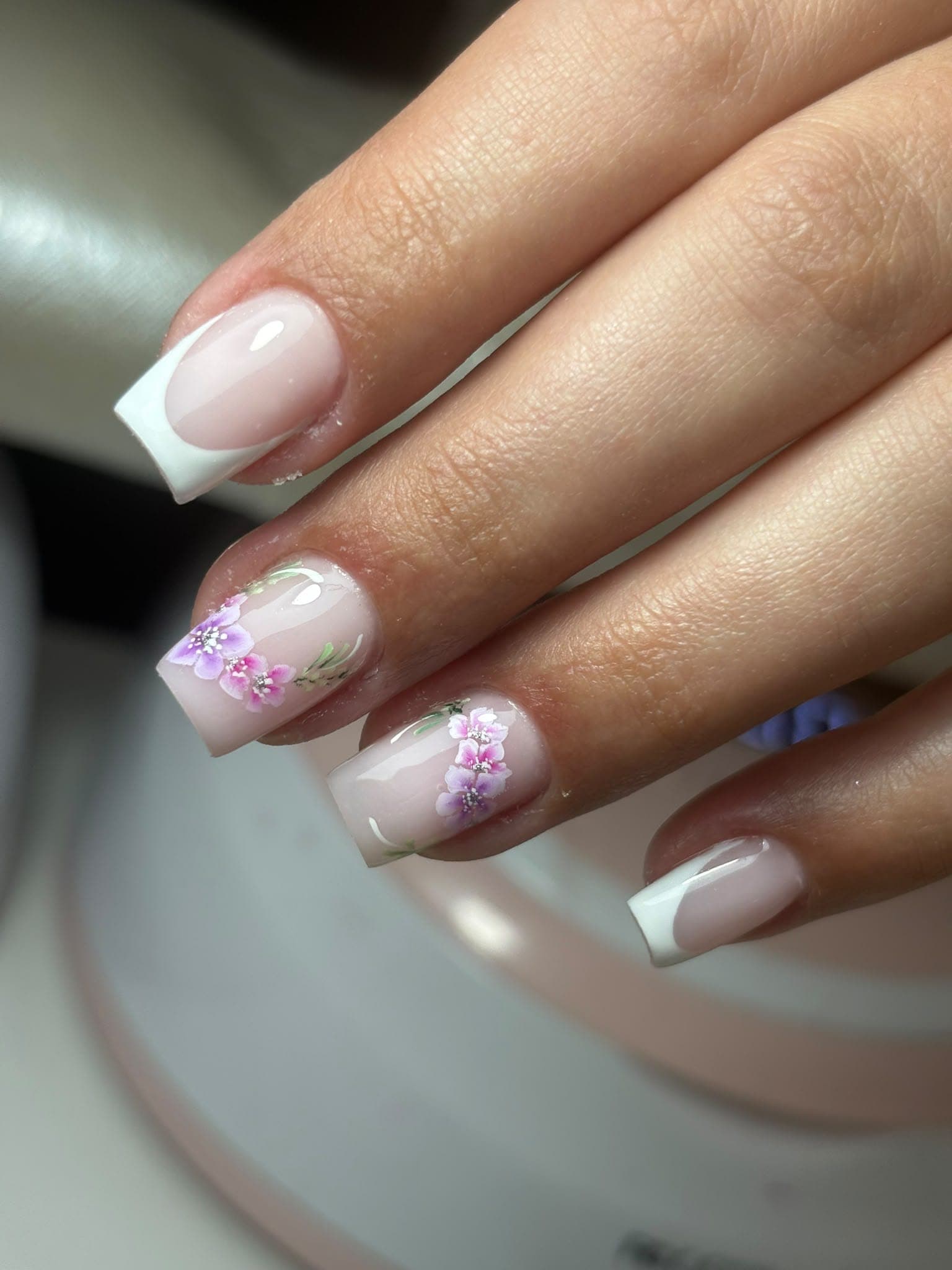 Unhas curtas ovais com efeito cromado holográfico e flores brancas e amarelas pressionadas