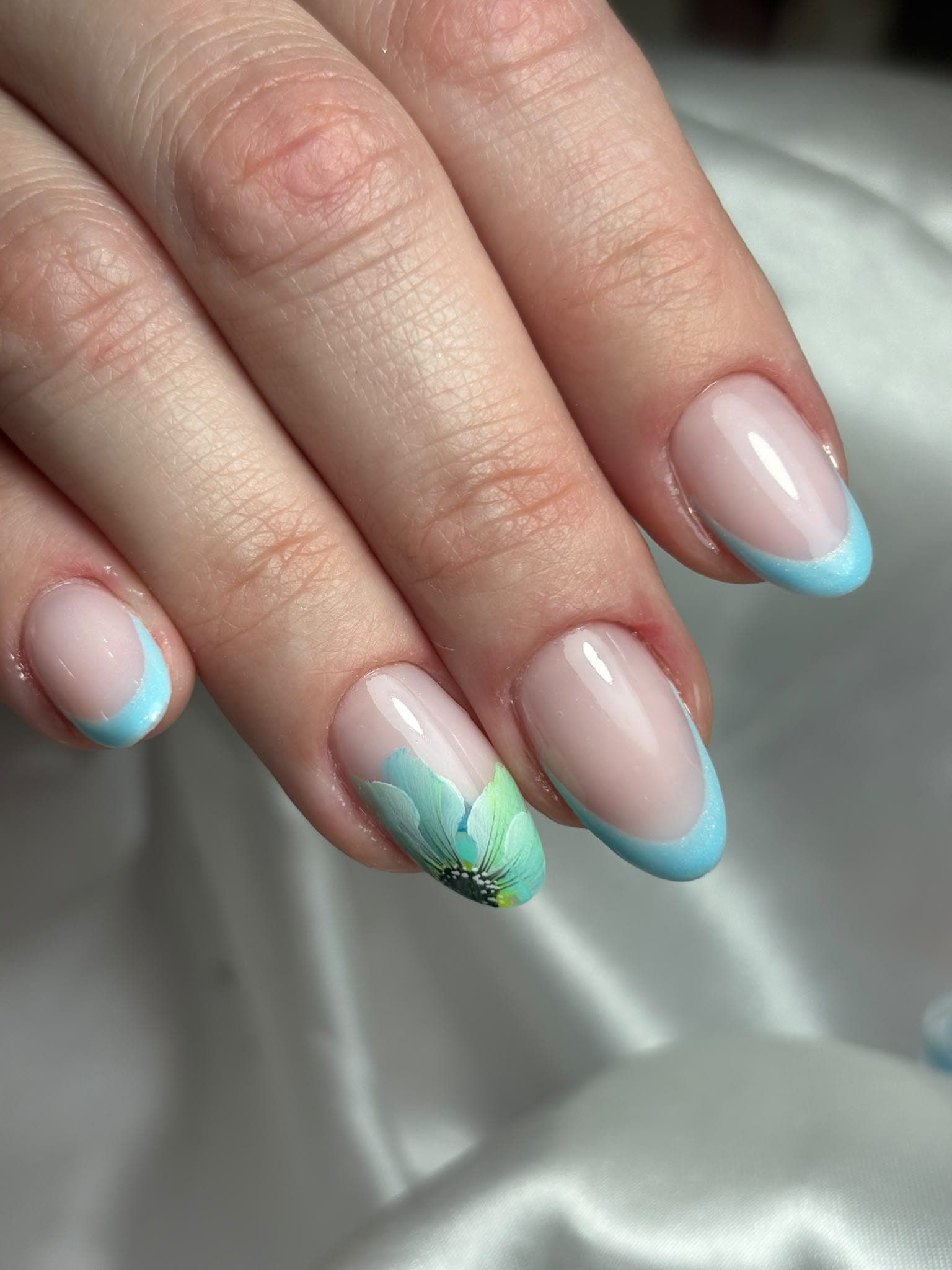 Unhas em amêndoa com base nude, pintura floral em roxo, azul e rosa e pontas em bordô